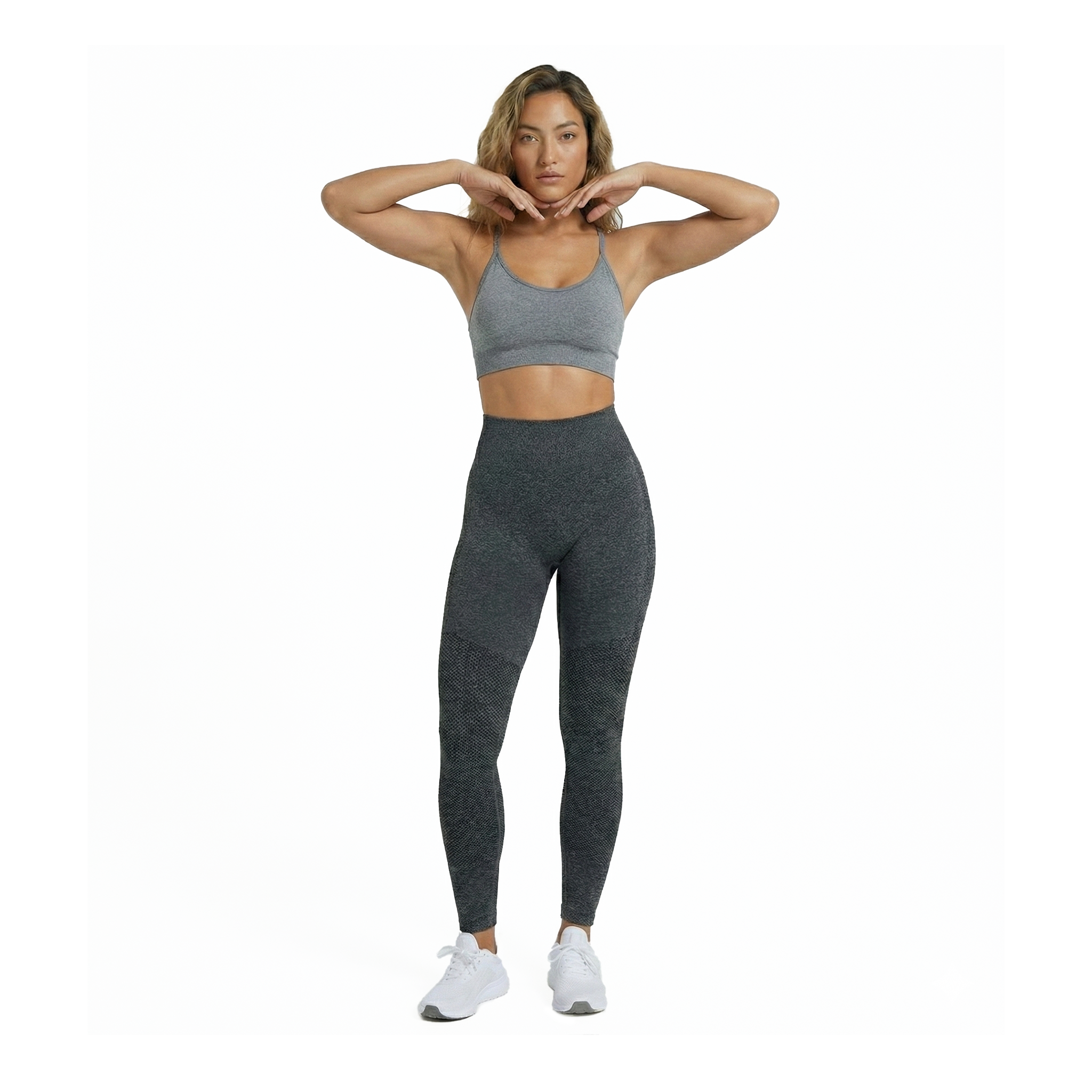 Woman wearing a gray sports bra and leggings on a white background, front view